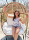 Woman wearing floral halter swim top and solid color bikini bottom sitting on an egg patio chair