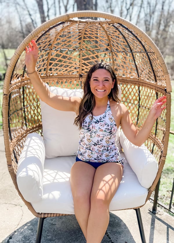 Woman wearing floral halter swim top and solid color bikini bottom sitting on an egg patio chair