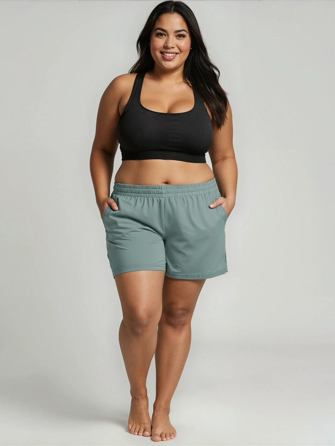 Woman wearing a black sports bra and light green shorts on a plain background