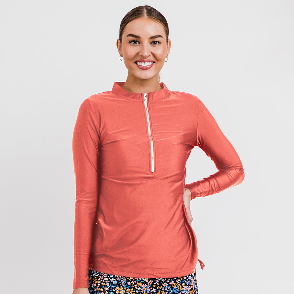 Smiling woman wearing a rust-colored Half-Zip Nora Swim Top | Final Sale with long sleeves and a front zipper, styled with floral swim bottoms, showcasing size-inclusive, modest, supportive swimwear designed for every body with a comfortable fit.