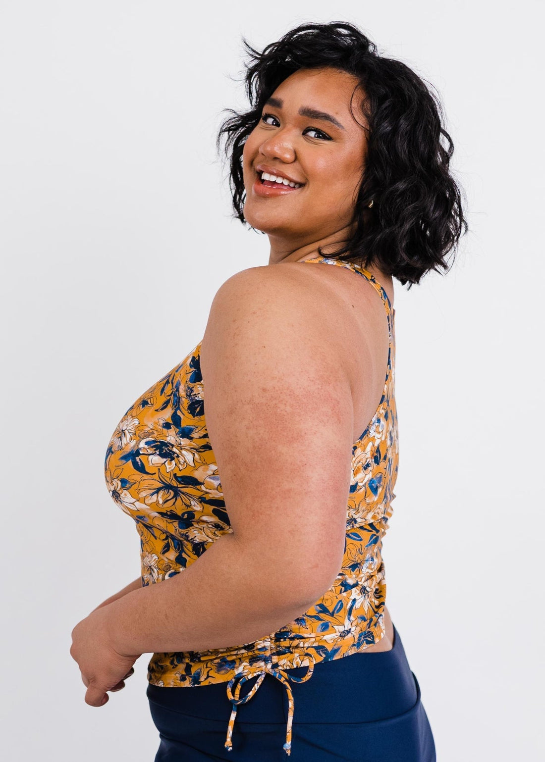 Woman wearing a yellow floral sleeveless top against a white background