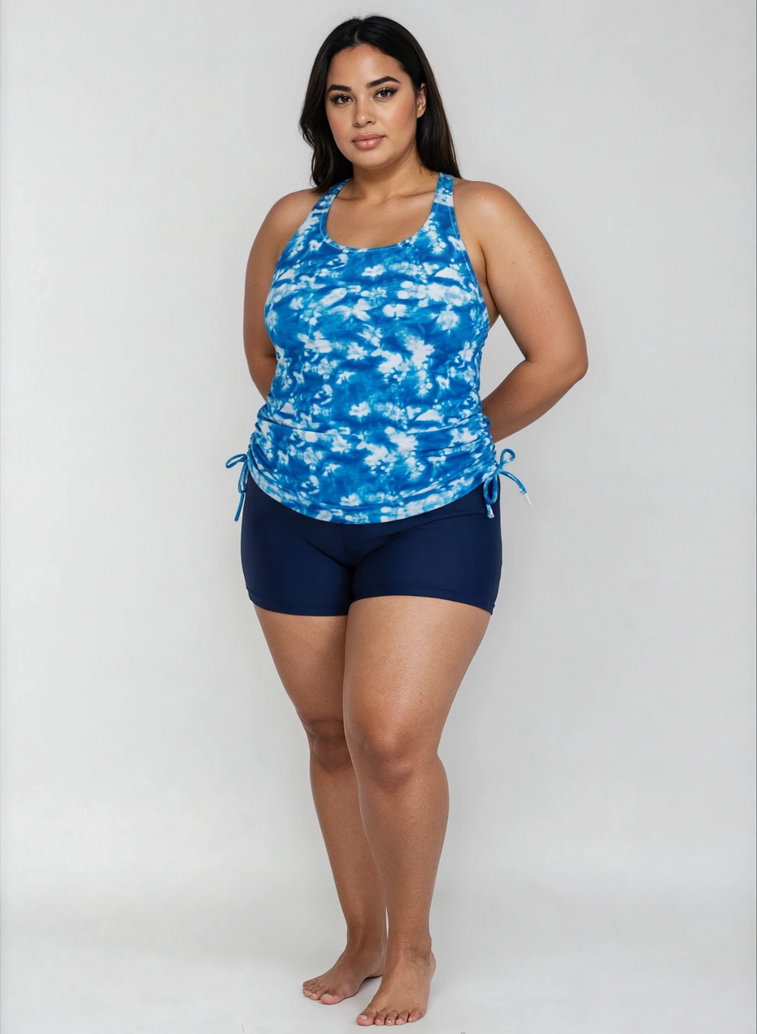 A woman modeling a blue and white tie-dye halter tank top with matching navy blue swim shorts against a light gray studio background.