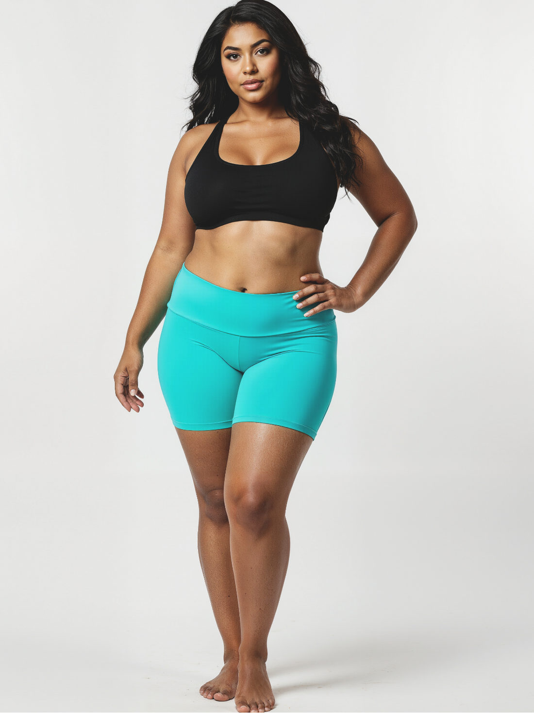 Woman wearing a black sports bra and teal shorts on a white background
